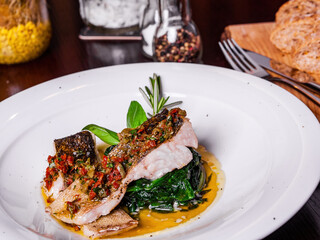 White fish in creamy sauce with spinach on a white plate