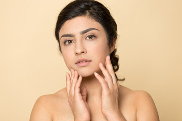 Close up portrait of young beautiful Indian woman isolated on yellow studio background touch healthy glowing skin after facial salon treatment. Millennial mixed race female after skincare procedures. - Powered by Adobe