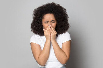 Unhealthy young African American woman isolated on grey studio background suffer from cold or fever blow running nose. Unwell mixed race female struggle with cvid-19 feel sick. Virus concept.