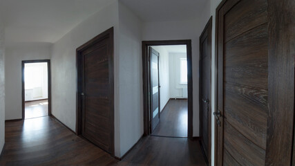 Panoramic photo of the apartment corridor with white walls, dark wooden doors and dark laminate flooring.