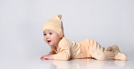 adorable laughing little kid in a yellow cotton jumpsuit and a hat is lying on the floor and trying to crawl. on white background. Happy childhood concept