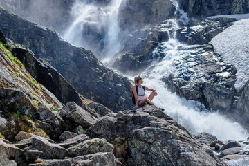Beautiful blonde tourist is sitting on a rock above the Siklawa waterfall in the Polish Tatra Mountains.