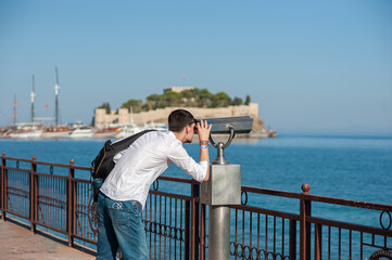 A happy tourist is watching trough a coin-operated binoculars in Kusadasi, Turkey