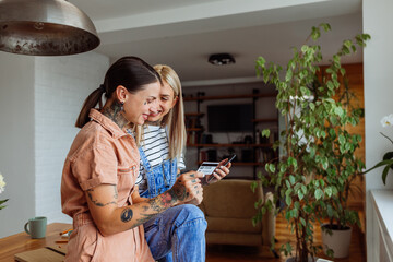 Young affectionate lesbian couple shopping online via cellphone and credit card