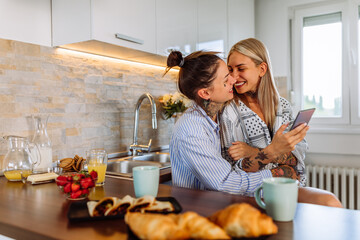 Women lgbtq couple in the kitchen using cellphone