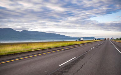 Big rigs semi trucks with semi trailers transporting cargo running on the straight divided highway at opposite directions