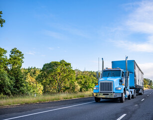Fototapeta na wymiar Blue day cab classic big rig semi truck transporting cargo in blue semi trailer moving on the straight highway at sunny day
