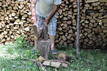 Lumberjack chopping wood with an ax in the yard and pile of cut stumps in the background on a summer day. Close up and copy space