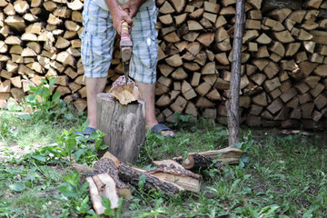 Man chopping wood with an ax in the yard and a large pile of cut stumps in the background. Close up and copy space