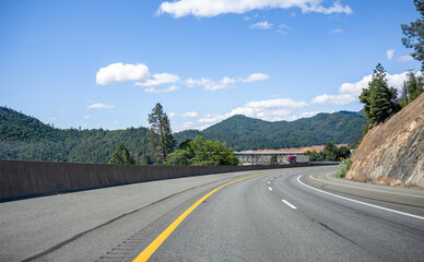 Fototapeta premium Burgundy big rig semi truck with refrigerator semi trailer running on the overpass road with bridge across the Shasta Lake
