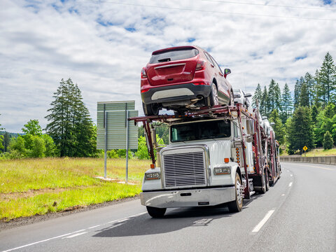Capacious car hauler big rig semi truck transporting cargo on modular semi trailer driving on the summer highway road
