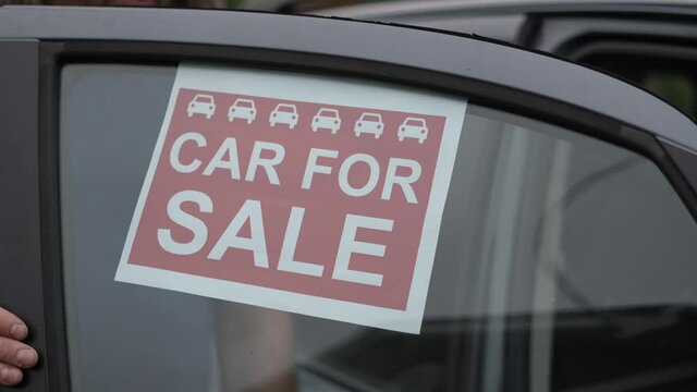 A man is placing a car for sale sign in the window of his car waiting for somebody to by his vehicle