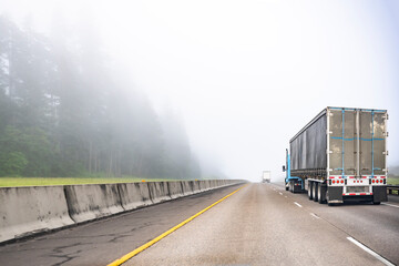 Convoy of big rigs semi trucks with semi trailers transporting cargo driving on the divided highway...
