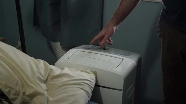 Man turning his portable AC air conditioner device ON. in his bedroom