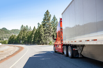 Industrial freight red big rig semi truck transporting cargo in dry van semi trailer driving...