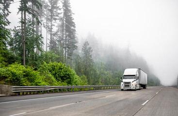 Industrial standard big rig white semi truck transporting cargo in dry van semi trailer running on...
