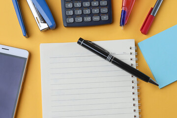 View from above on a blank notebook, pen, notepad, calculator, stapler, cell phone, on the yellow background