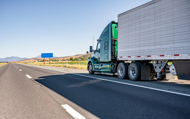 Powerful big rig green semi truck transporting cargo in refrigerator semi trailer moving on the...
