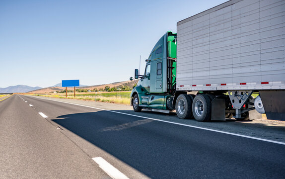 Powerful big rig green semi truck transporting cargo in refrigerator semi trailer moving on the straight highway road leaning against the horizon