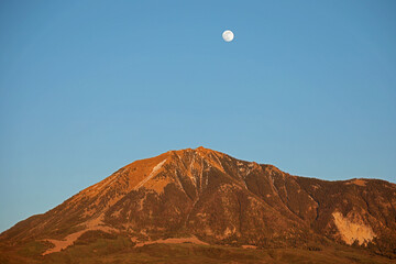 Rising moon in the evening sky over the orange mountain.