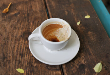 A finished white cup of espresso stands on a wooden table.