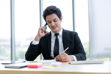 Smart and good looking Asian young businessman talking on the cellphone in the office.