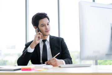 Smart and good looking Asian young businessman talking on the cellphone in the office.