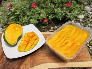 Mango Cheese Cake in Container and Peeled Mango on Wooden Board with Flower Background. Blurry Background