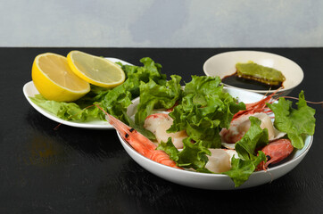 Natural raw scallop with boiled shrimp in the sink in a ceramic bowl with lettuce leaves and sauce on a dark background.
