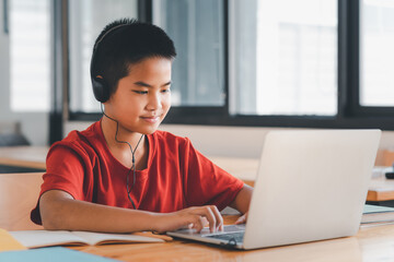 Young Asian man student wearing headphones studying online using laptop at home.