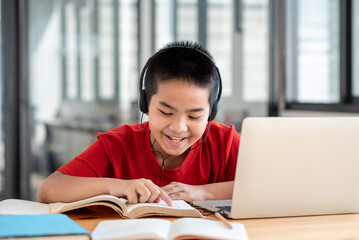 Schoolboy Asians are happy to study with headphones pointing to a book in the room.