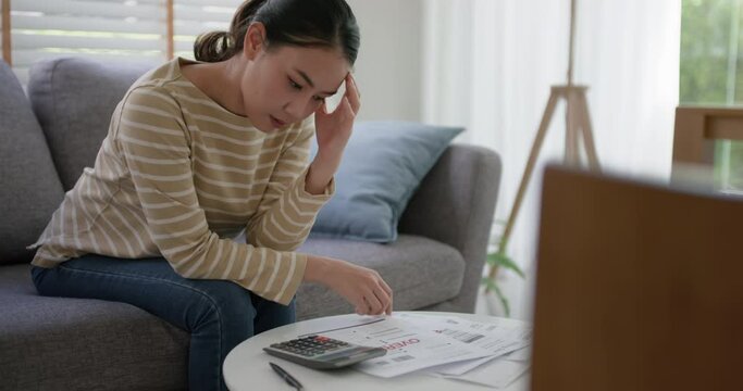 Upset tired young asia sad lady people sit sofa couch at home think hard worry in tax expense saving issue past due loan late payment on covid impact life feel grief pensive struggle in money lost.