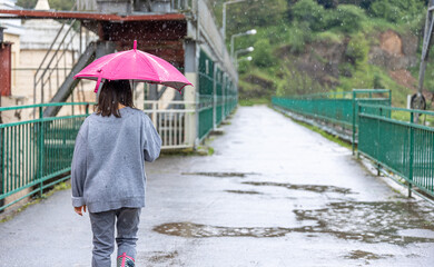 Back view of a girl under an umbrella on a walk in the rain.