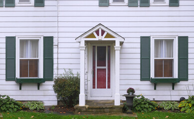 Modest white clapboard house with green shutters around windows