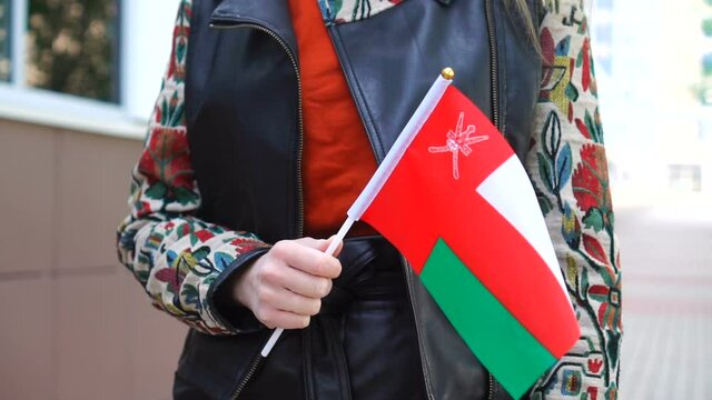 Unrecognizable woman holding Omani flag. Girl walking down street with national flag of Oman
