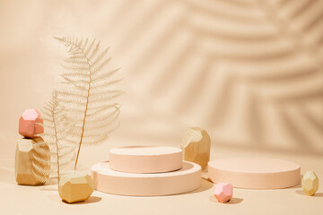 Composition of  geometric podiums, balancing wooden stones and dried leaves for products presentation or exhibitions. Tropical leaf shadow on sand color background