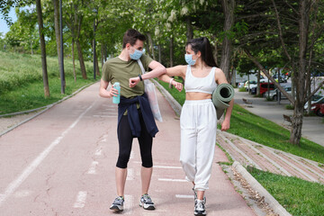 Couple in sport clothes wearing masks and greeting with elbows bumps