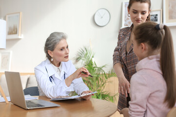 Fototapeta premium Mother and child in the doctor office meeting the pediatrician, they are sitting at desk in hospital.