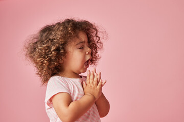 Adorable girl sneezing with open mouth on pink background