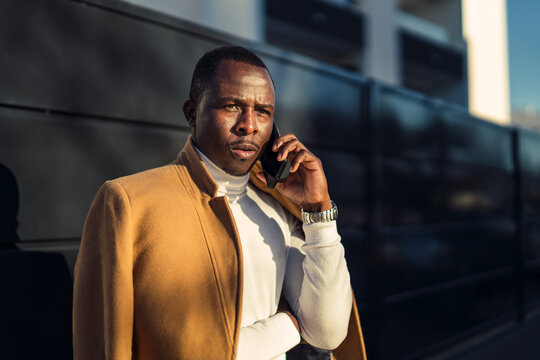 Thoughtful young black guy talking on smartphone on street