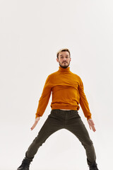 a man in an orange sweater spread his legs shoulder-width apart and gestures with his hands