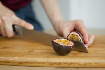 Female hands is cutting a fresh ripe passion fruit, maracuya on a cut wooden board. Exotic fruits, healthy eating concept