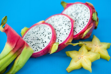 Slices of dragon fruit or pitaya with pink skin and white pulp with black seeds on blue background. Exotic fruits, healthy eating concept