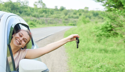 Young happy woman is sitting in the car, holding the keys in her hand. The girl is happy with the...