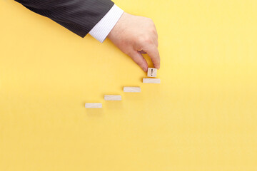 A businessman's hand is adding a wooden cube to the top of the stairs