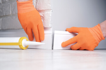 Installation of skirting boards, master glues  floor plinth to  outer corner of  wall, hands in...