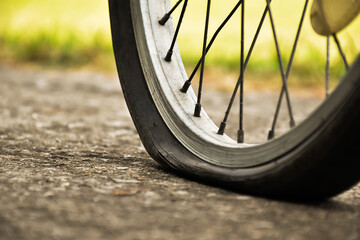 Close up view of bike which has flat tire and parked on the pavement, blurred background. Soft and selective focus on tire.