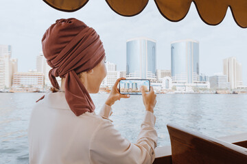 Happy asian woman in a red turban takes pictures on her smartphone while cruising on a traditional...
