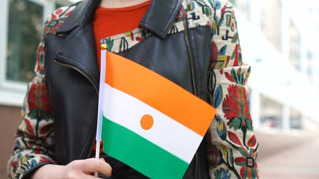 Unrecognizable woman holding Nigerien flag. Girl walking down street with national flag of Niger