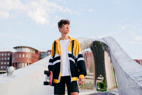Caucasian teenager with skateboard standing on the bridge in the city